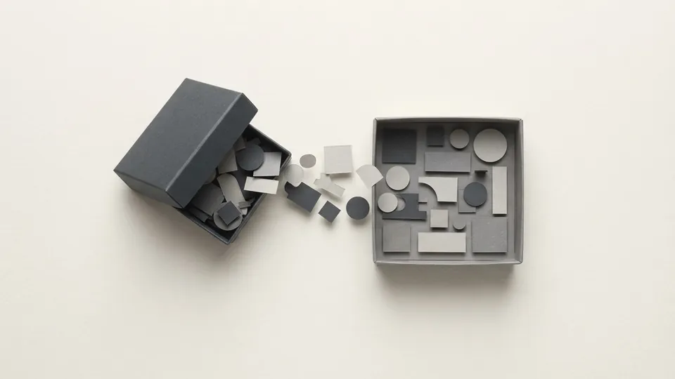 A graphite paper box tipped open with its paper pieces moving across into a second box that is being neatly filled