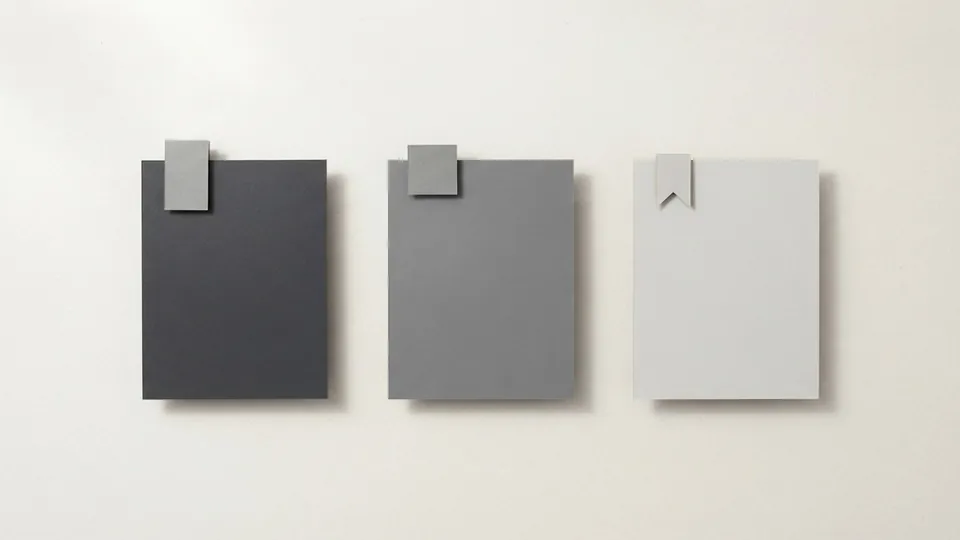 Three paper cards in graphite, mid grey and pale grey, each with a different small blank tab clipped to its top edge