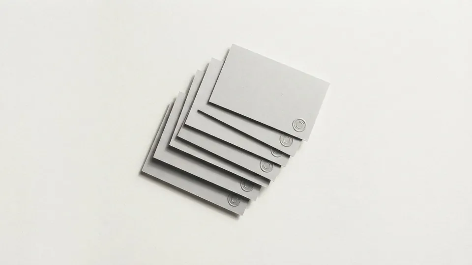 A fanned stack of pale grey paper cards, each with a tiny embossed seal in its corner