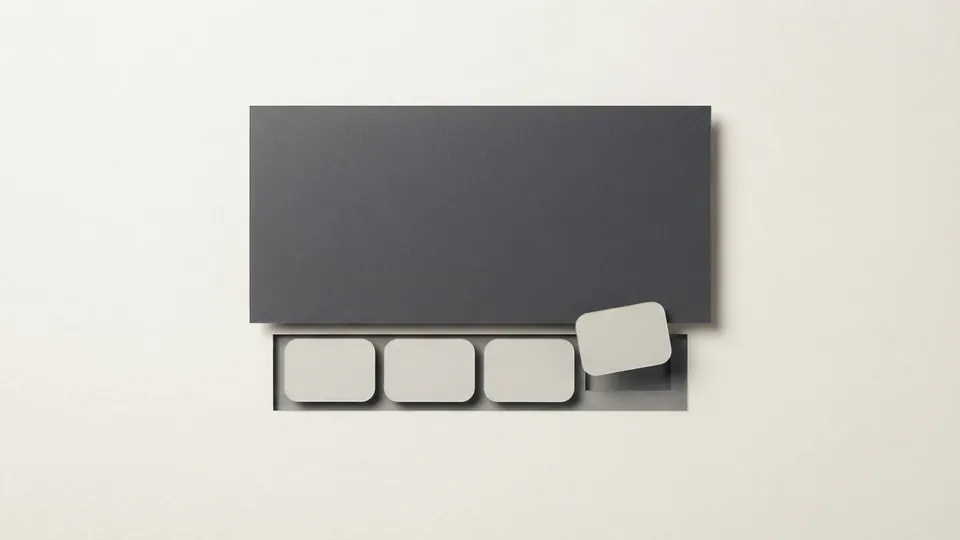 A dark paper panel with four pale rounded paper tiles set into a recessed strip below it, the last tile being slotted in