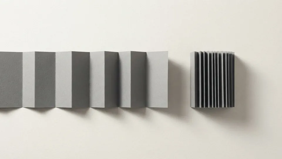 A long grey paper strip unfolded in wide pleats beside the same kind of strip folded tightly into a short compact block