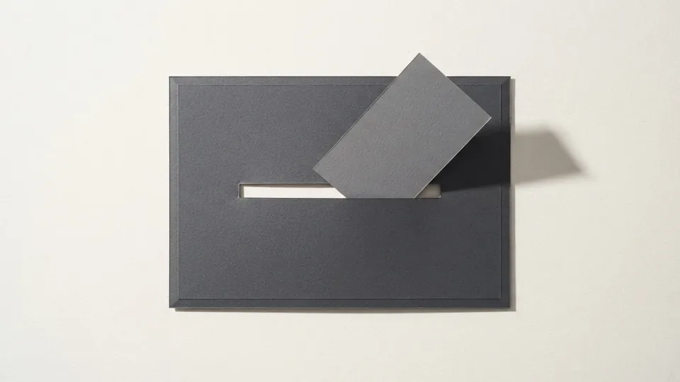 A graphite paper sheet with a slot cut in it and a smaller grey card popping up out of the slot, casting a long shadow