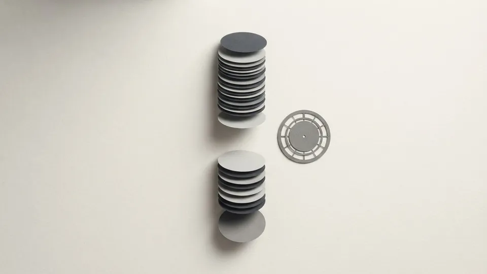 A column of paper discs split by a gap as if frozen mid-fall, beside a small numberless paper clock face