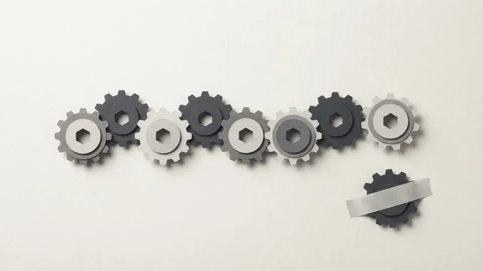 A working row of paper cogs with one cog set aside below it, a strip of pale paper tape stuck across it