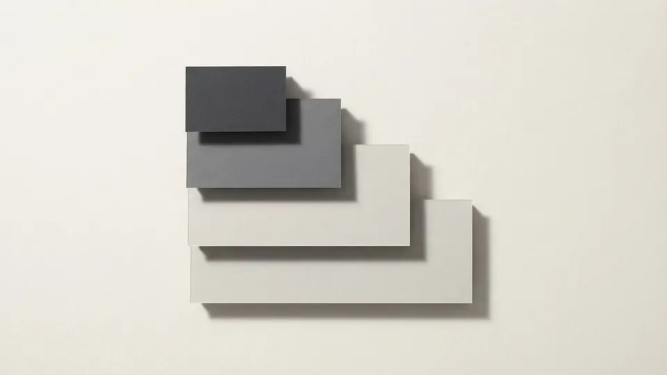 Four stacked paper blocks stepping down like a staircase, the top block darkest graphite and each lower one paler